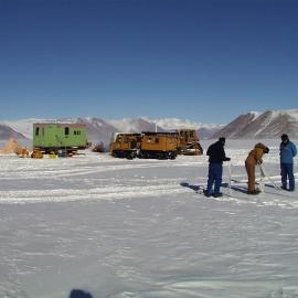 Person on sled on textured snow with scientific equipment on sled.  Green portacabin in background