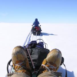 Close up of boots and front of sled being pulled behind a skidoo making new tracks