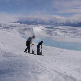 Two people with equipment in middle distance, by ice lake