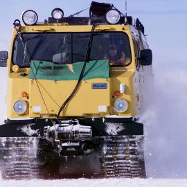 A Hagglunds tracked vehicle travelling in Antarctica, survival bags and bridging gear (for crossing large ice cracks) on top