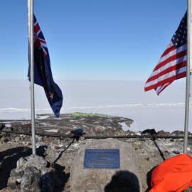 Scott Base seen between NZ, US flags and plaque for the wind farm