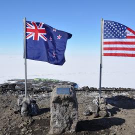 Scott Base seen between NZ, US flags and plaque for the wind farm
