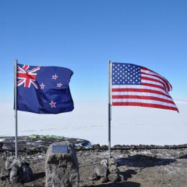 Scott Base seen between NZ, US flags and plaque for the wind farm