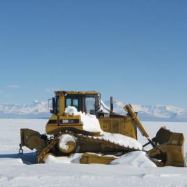 CAT (Caterpillar) bulldozer covered in snow with mountains behind