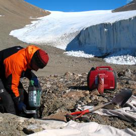 Peter Almond attacks ice cemented material with an impact drill. Howard Glacier is in the background. Eastern Taylor Valley.