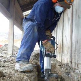 Heritage carpenter Tank Adams, digging a trench for a sub-surface dam to prevent melt water ingress at Discovery Hut