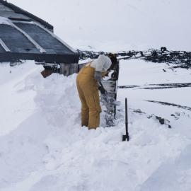 Chris Adams shovelling snow from entrance of Scott's Hutt, Cape Evans
